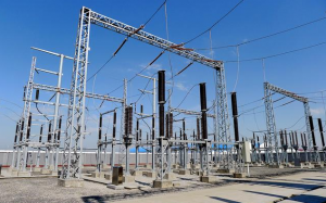 The substation is located on a wide site surrounded by towering pylons. The pylons are densely covered with power transmission lines, intertwined to form an intricate network.