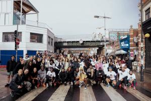 Photo capturing diverse group of over 100 smiling runners posing together on a street in London at a Nike event, with running coach in the center of the group holding up a megaphone.