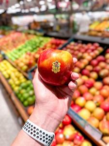 A ripe SugarBee® apple held in someone's hand in front of a grocery store display full of apples.