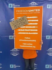 Person holding a sign at #MyFreedomDay event with Freedom United's logo and hand written note to "sign our petition!"