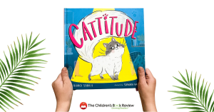 A small child's hands holding a copy of the picture book Cattitide. Leaves are seen in the background on either side of the book.