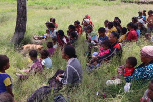 Displaced indigenous West Papuans sit in a field