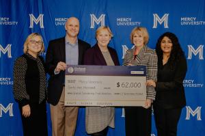 Oxford International Education Group and Mercy University officials pose in front of a large cardboard check symbolic of the $62,000 donation made to the university
