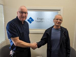 Stephen Frost of Engineering Foundry Supplies and Andrew Montgomery of Montgomery Signs Ltd shaking hands in front of their companies' logos, symbolizing their successful acquisition partnership.
