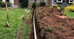 Photo of a narrow trench containing a pipe that has been installed in a lawn.