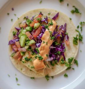 Grilled fish on corn tortilla, topped with vibrantly colorful cabbage, pico de gallo salsa and a drizzle of sauce