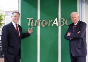 Two impeccably dressed gentlemen are standing in front of the TutorABC logo, posing for a photo.