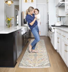 Woman holding child in designer kitchen while standing on a 30-inch by 108 inch GelPro Elite Comfort Floor Mat in the Teagan Sunny Citrus design.