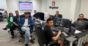 The Dingdoor team, elated by growth news, sits around a conference table in Miami, surrounded by professional workstations.