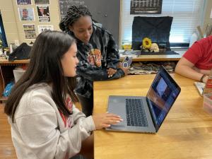 Two upper school students collaborate on a project using online research and creation tools on a laptop computer.