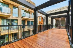 A chic balcony adorned with rich brown decking and sleek black metal railings offering picturesque views of neighboring apartment decks.