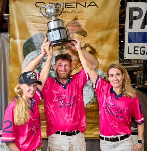 Three arena polo players hold up polo trophy