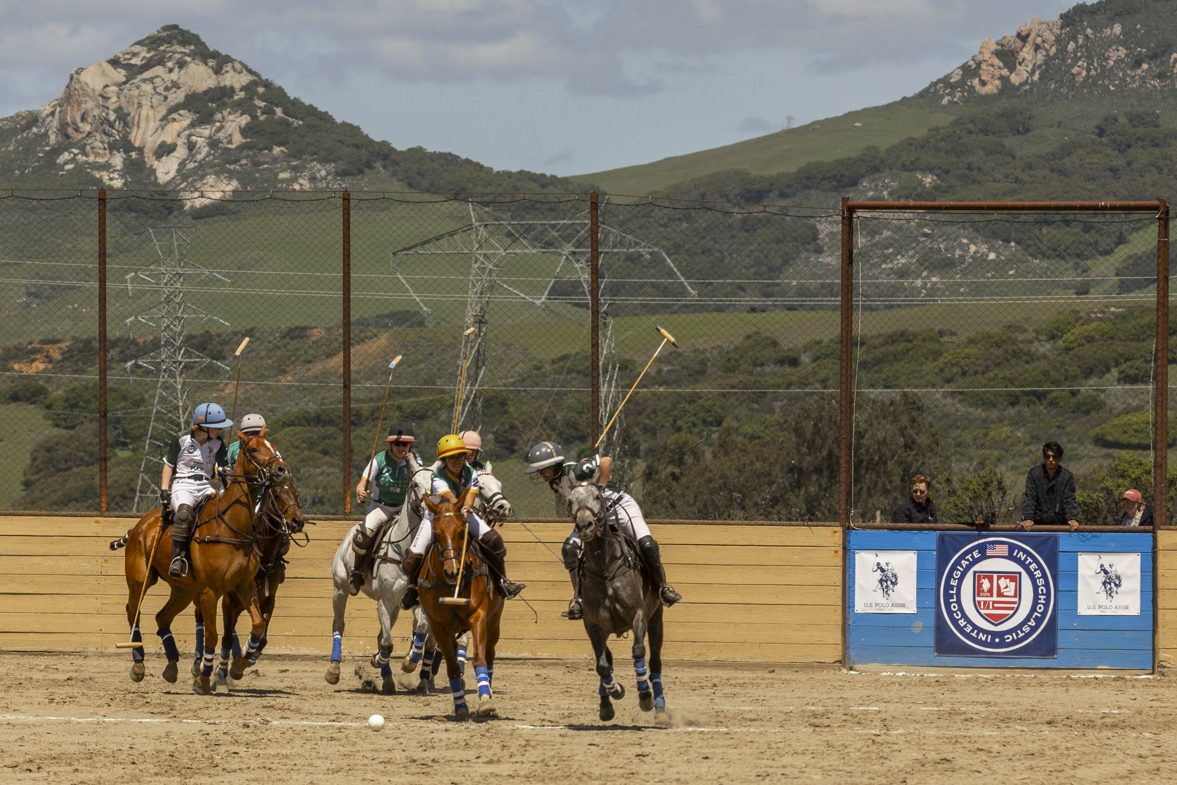 6 polo players ride on horseback in arena with mountains in the background