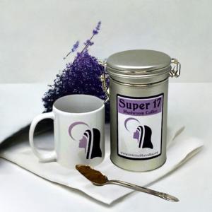 a tin of mushroom coffee, a mug with the sisters' logo, and a teaspoon laying with the powder in it