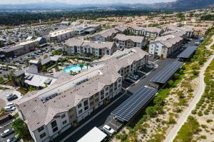 A drone shot of some solar carports with a nice apartment complex behind them.