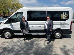 Image: Nancy Vargas, CEO, and Mike Vargas, COO of DH2 Chauffeured Transportation, stand at opposite ends of a white transit van. The van displays the DH2 logo and text that reads 'The New Terminal One'.