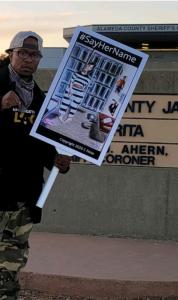 MinisterKingXPyeface holding a C-Note #SayHerName protest poster in front of the Alameda County Santa Rita Jail