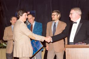 Dean Wesley Smith being congratulated by Algis Budrys in a tuxedo, with (l to r) Robert Silverberg, Roger Zelazny, and Dr. Gregory Benford behind at the 1985 Awards Ceremony at Chasen's Restaurant in Beverly Hills.