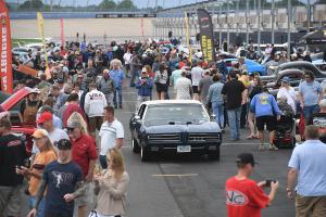 Vintage cars surrounded by people on the speedway