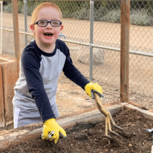 A young boy wearing specs and smiling while digging some soil.