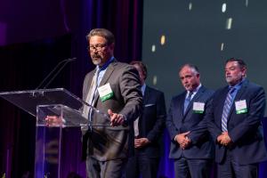 Tempest Energy’s VP of Customer Relations Adam Guillory (with CEO Bill Cain (l) and COO Mike Zappone (r) in background) thanks Entergy’s judges, employees, and guests after accepting the Premier Supplier Storm Response Award in New Orleans on May 14.