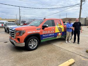Two men shake hands in front of a colorful truck with a Pelican Paint Group vehicle wrap, designed by Louisiana Graphics, showcasing their professional vehicle wrap service.