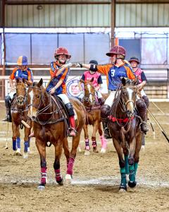 A young up-and-coming female arena polo player fist bumps her teammate after a win.  both are on horses
