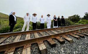 eight sisters standing between the railroad tracks and the ocean
