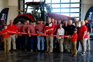 Redline equipment employees stand in front of a large tractor as they cut a ribbon to commemorate the opening of their new facility.