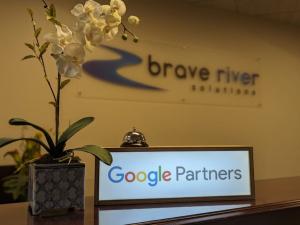 The google partners sign sits on the reception desk at the Brave River office, with the Brave River Solutions sign displayed on the wall in the background