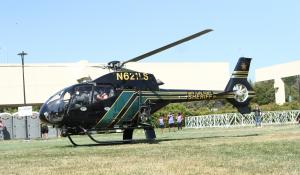 A black and green helicopter landing outside on green grass.