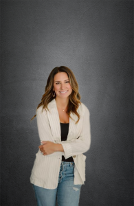 Planet Home Lending Mortgage Loan Originator Melissa Couvillion wearing a white jacket and blue jeans and leaning against a wall.