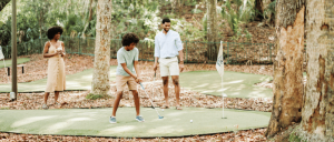 A family enjoying a game of mini golf surrounded by trees in the forest.