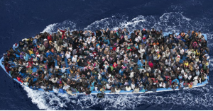 A bird's eye view of a boat at sea packed with people whose faces are looking up at the camera