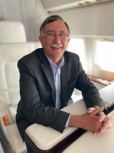 A man smiles at the camera while sitting inside an executive jet