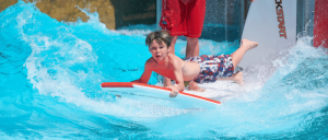 A young boy rides a bodyboard on a wave at Water World, smiling and having fun.