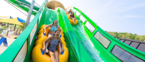 A group of friends laughs and enjoys a thrilling ride down a green water slide at Water World.