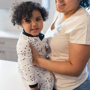 A mother holding her smiling young child, who is wearing star-patterned Burt's Bees Baby pajamas.
