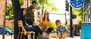 A family of four with their dalmatian dog sitting on a bench outside a restaurant, smiling and enjoying a meal together.