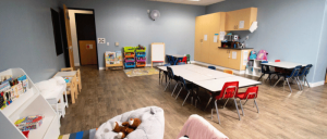A brightly lit classroom with tables, chairs, toys, and educational supplies neatly organized for children's activities.