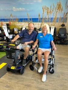 Photo of Owners Tim and Vickie Maatouk siting on a Zoomer power chair and Pride Victory scooter ready to help with mobility equipment solutions that provide comfort and convenience