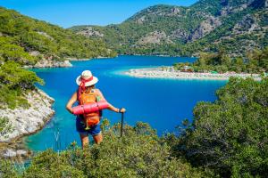 Woman hiker standing on cliff with backpack and poles, admiring blue lake. Hiking routes.