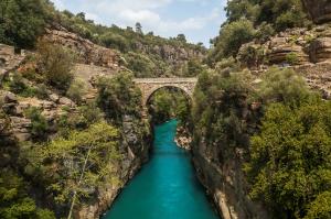 Serene image of a bridge over a river, framed by verdant trees, providing a tranquil setting for hikers in Antalya Canyon.