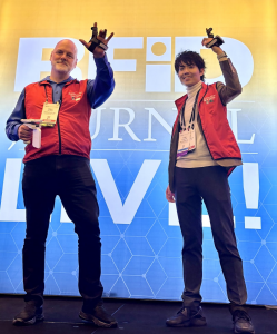 Two men on stage holding wearable scanners for RFID