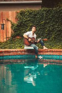 Dylan sitting by a beautiful clear blue pool with his acoustic guitar