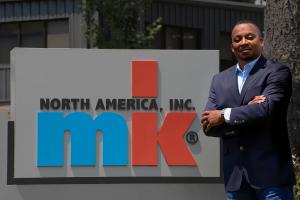 An image of Damon Neal standing outside of mk North America's headquarters next to an mk sign.