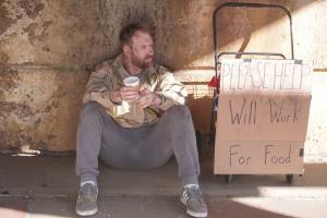A homeless veteran leans against a concrete wall.