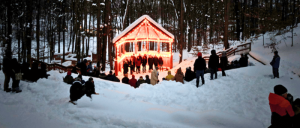 People gathered in the snow near a house with a red light.