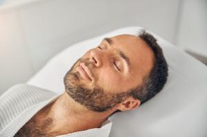 A young man with a short beard sits calmly at a wellness center, awaiting treatment for Upper Airway Resistance Syndrome (UARS).