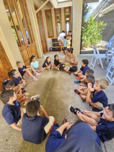 Young students whose school burned down in the Lahaina fires sit together in a circle to hold a weighted therapeutic teddy bear called a Comfort Cub, from San Diego’s The Comfort Cub nonprofit.